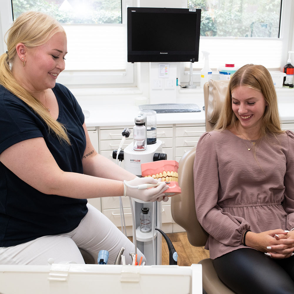 Eine Mitarbeiterin zeigt einer Patientin eine Zahnmodell